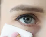 Delikatne łzawienie jednego oka, z widoczną łzą przy kąciku, podczas gdy chusteczka delikatnie ją osusza.