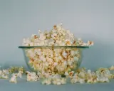 Góra popcornu w szklanej misce, rozsypane ziarna wokół. Ile popcorn kcal?