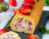 Un roulé aux fraises moelleux, garni de crème et de morceaux de fraises fraîches, décoré de fraises entières.