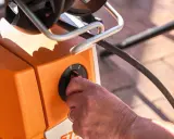 Hand dreht Schalter am orangefarbenen Hochdruckreiniger. Vorbereitung zum Anschluss an den Wasserhahn.
