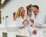 Para relaksu w hotelach spa w Polsce. Uśmiechnięta para w szlafrokach wznosi toasty szampanem na balkonie.