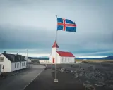 Islandia praca: biały kościół z czerwoną wieżą i flagą Islandii na tle pochmurnego nieba.