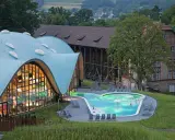 Moderne Therme mit geschwungenem Dach und beleuchtetem Pool, daneben historische Gebäude.