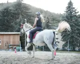 Reiterin auf weißem Pferd im Trab, um die Halsmuskulatur des Pferdes zu lockern.