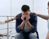 Mężczyzna z rękami na twarzy, otoczony przez osoby wspierające go w walce z narkomanią.