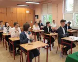 Uczniowie siedzą w ławkach podczas egzaminu. Zastanawiają się, ile trwa matura z biologii, skupieni na zadaniach.