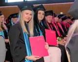 Absolwentki w togach i biretach Akademii WSB, z dyplomami w rękach, świętują zakończenie studiów na kierunku filologia angielska.