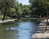 Un día soleado en las piscinas naturales de La Codosera. Personas disfrutan del agua fresca, una nada mientras otras pasean por la orilla.