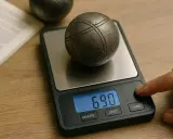 Une boule de pétanque sur une balance numérique affiche 690. Le poids de la boule est mesuré.
