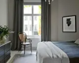 Sovrum med en säng, en stol och en byrå. Konst av Sofia Wallenstam på väggen.