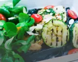 Kolorowy catering dietetyczny z grillowaną cukinią, pomidorkami i zielonymi liśćmi. Dowiedz się, jak podgrzewać catering dietetyczny, by zachować świeżość.