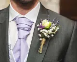 Elegancka butonierka w marynarce, ozdobiona białymi kwiatkami i lawendą, dodaje uroku ślubnemu strojowi.