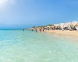 Spiaggia affollata con lettini e ombrelloni bianchi, gente che nuota e prende il sole. Un'immagine perfetta delle località balneari Puglia.