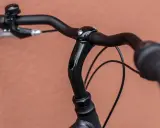 Czarne kierownica i mostek roweru, widoczne momenty dokręcania śrub. Dzwonek i hamulec po lewej.