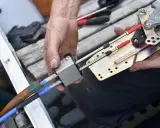 Main d'un mécanicien démontant le boîtier de commande d'un bateau, révélant les câbles et le mécanisme.