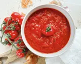 Eine Schüssel mit köstlicher, hausgemachter italienischer Tomatensauce, garniert mit einer frischen Kirschtomate. Daneben liegen frische Tomaten und Zwiebeln.