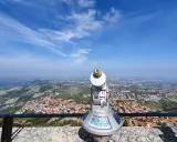 Telescopio con vista panoramica su cosa vedere a San Marino. Il paesaggio collinare e la città si estendono sotto un cielo azzurro con nuvole sottili.