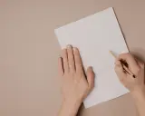 Ręce piszą list motywacyjny po angielsku na białej kartce.