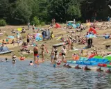 Tłumy ludzi wypoczywają na plaży nad jeziorem Chechło. Woda jest pełna kąpiących się, a na brzegu opalają się plażowicze.
