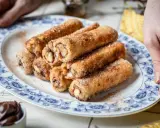 Nutella French Toast Rolls, goldbraun gebacken und mit Zimt-Zucker bestreut, auf einem Teller mit blauem Blumenmuster.