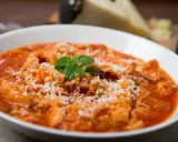 Trippa alla romana, uno dei piatti tipici del Lazio, servita in una ciotola bianca con parmigiano grattugiato e una fogliolina di menta.