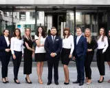 Grupa profesjonalistów w eleganckich strojach stoi przed nowoczesnym budynkiem.