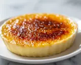 Crème brûlée à la vanille avec une croûte caramélisée dorée sur une assiette blanche.