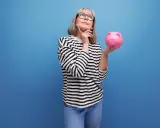 Mujer pensativa con hucha rosa, considerando los tipos de planes de pensiones para su futuro.