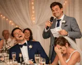 Un hombre da un discurso gracioso para bodas de oro, mientras la pareja ríe a carcajadas.