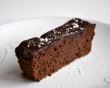 Wilgotny brownie z czerwonej fasoli, polany czekoladą i posypany cukrem pudrem, na białym talerzu z serduszkami.