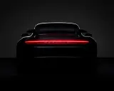 Ein schwarzer Porsche von hinten, dessen Rückleuchten in einem leuchtenden Rot erstrahlen und den Schriftzug "PORSCHE" beleuchten.