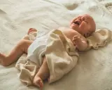 Płaczące, dwuletnie dziecko się pręży i napina, owinięte w jasny kocyk.