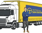 Hombre sonriente junto a un camión amarillo con logo de autoescuela. ¿Cuánto cuesta el carnet de trailer?