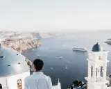 A man gazes at the caldera on a gay Greek island, with iconic blue domes and white architecture overlooking the Aegean Sea.
