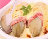 Deux endives braisées enveloppées de jambon, nappées de fromage fondu et gratiné, garnies d'une feuille de persil. Un plat réconfortant.