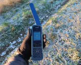 Ręka w rękawiczce trzyma telefon Inmarsat IsatPhone, gotowy do nawiązania połączenia przez telefonię satelitarną w mroźny poranek.