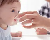 Ein Baby trinkt vorsichtig Wasser aus einem Becher, gehalten von einer Hand. Die Frage "ab wann Baby Wasser geben?" wird hier visuell beantwortet.