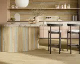Interni di una casa super moderna: isola cucina in legno e marmo, sgabelli grigi, mobili rosa cipria e pavimento in parquet chiaro.