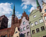 Kolorowe kamienice w Gdańsku pod błękitnym niebem z chmurami, w tle kościół.