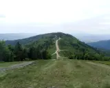 Droga wijąca się przez zielone wzgórza, prowadząca na szczyt Klimczok. W oddali widać pasma górskie.
