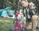 Mężczyzna pakuje plecak, przygotowując się do wyprawy. W tle rozstawiony namiot. Idealny zestaw, by wiedzieć, co zabrać w góry na 5 dni.