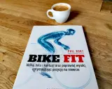 Książka "Bike Fit" z anatomicznym schematem rowerzysty i filiżanką kawy na drewnianym blacie.