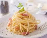 Un plat de tagliatelles carbonara crémeuses, garni de lardons et de persil frais, prêt à être dégusté.