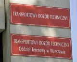 Dwa czerwone szyldy z białym napisem "TRANSPORTOWY DOZÓR TECHNICZNY". Dolny szyld zawiera dodatkowo "Oddział Terenowy w Warszawie". Miejsce, gdzie można uzyskać homologację.