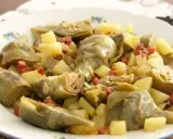 Plato de alcachofas tiernas y patatas cortadas en cubos, salpicado con trocitos de jamón. Un manjar casero.