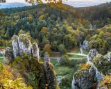 Jesienne barwy w Ojcowskim Parku Narodowym. Wapienne skały porośnięte mchem i jesienną roślinnością, otoczone lasem w odcieniach złota i zieleni.