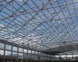 Estructura metálica de una **cercha Pratt** en construcción, con operarios trabajando en el techo bajo un cielo azul.