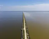 Un sentiero stretto divide due specchi d'acqua, uno scuro e uno più chiaro, sotto un cielo azzurro. Sembra la ciclabile degli angeli.