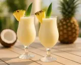 Deux verres de pina colada sans alcool, décorés d'ananas, avec un ananas et une noix de coco en arrière-plan.