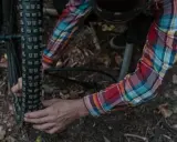 Rowerzysta w koszuli w kratę pompuje oponę rowerową na leśnej ścieżce.